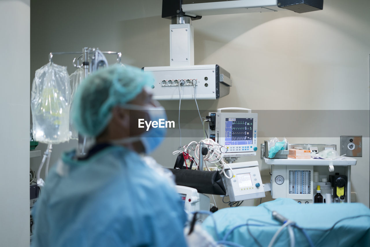 Blurred man in surgeon uniform looking away while conducting surgery in modern operating theater