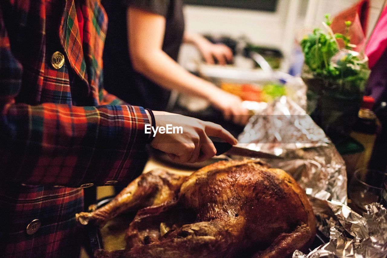 Midsection of person holding kitchen knife on thanksgiving turkey at home
