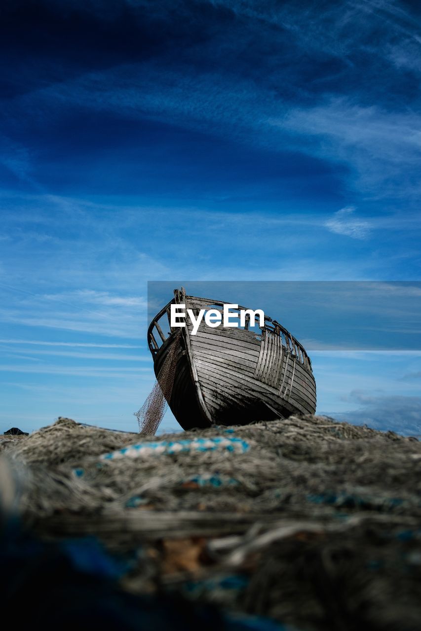 Low angle view of abandoned boat on beach against blue sky