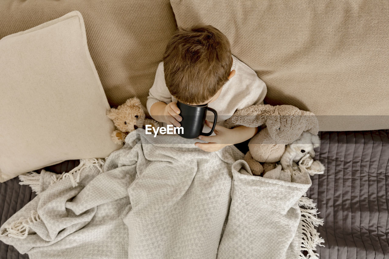 Sick little boy drinking hot tea on the bed at home. unwell, illness child wrapped in a blanket