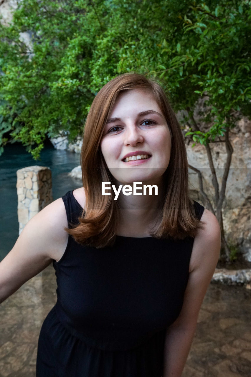 Portrait of beautiful young woman standing against trees