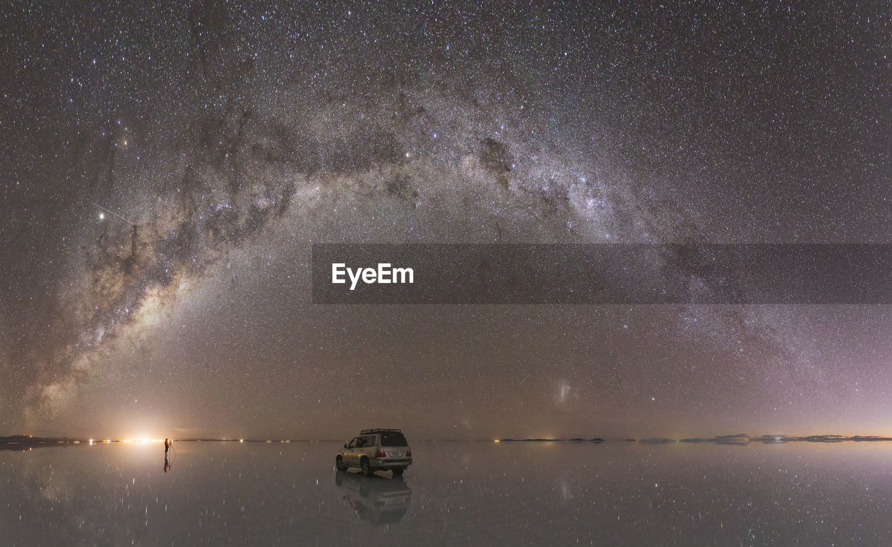 Car over water under the milky way in panoramic view