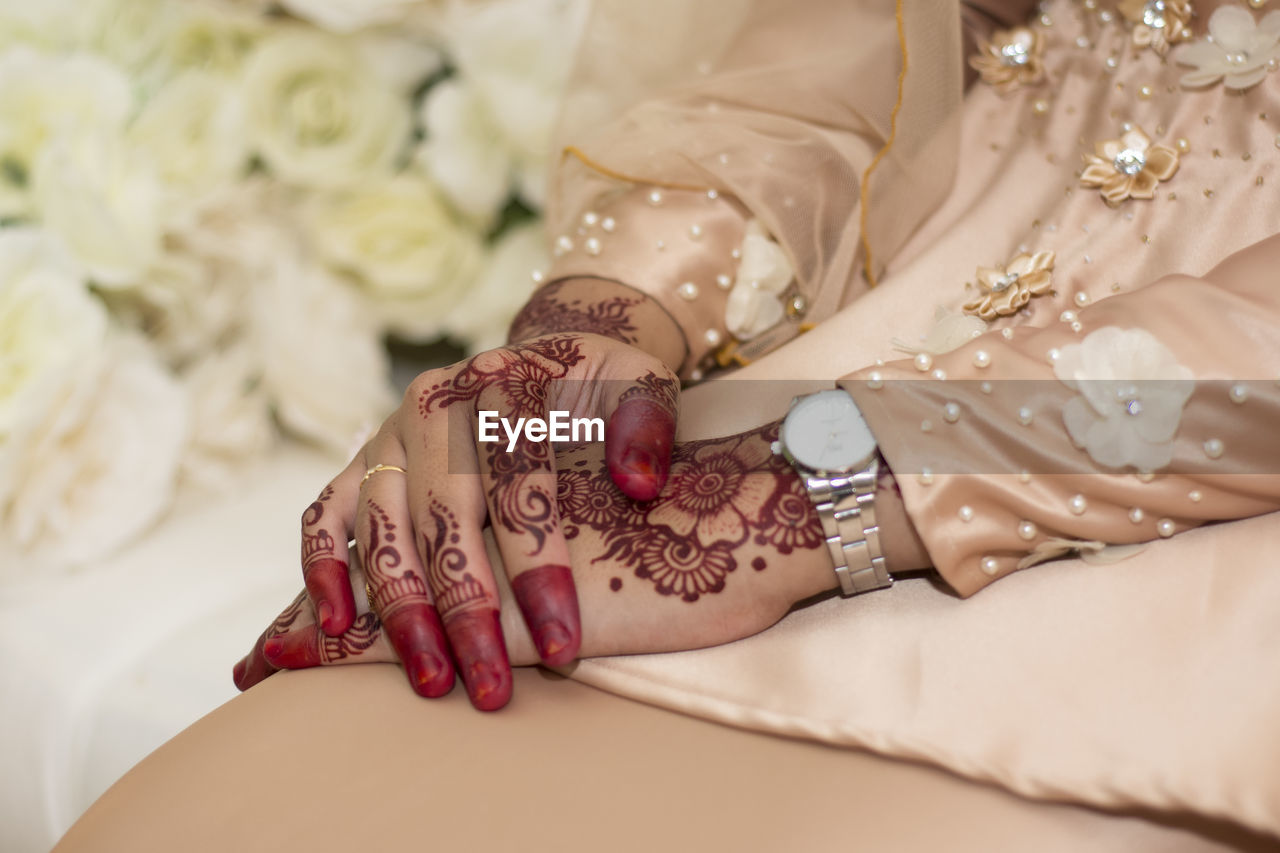Midsection of bride with henna tattoo on hand