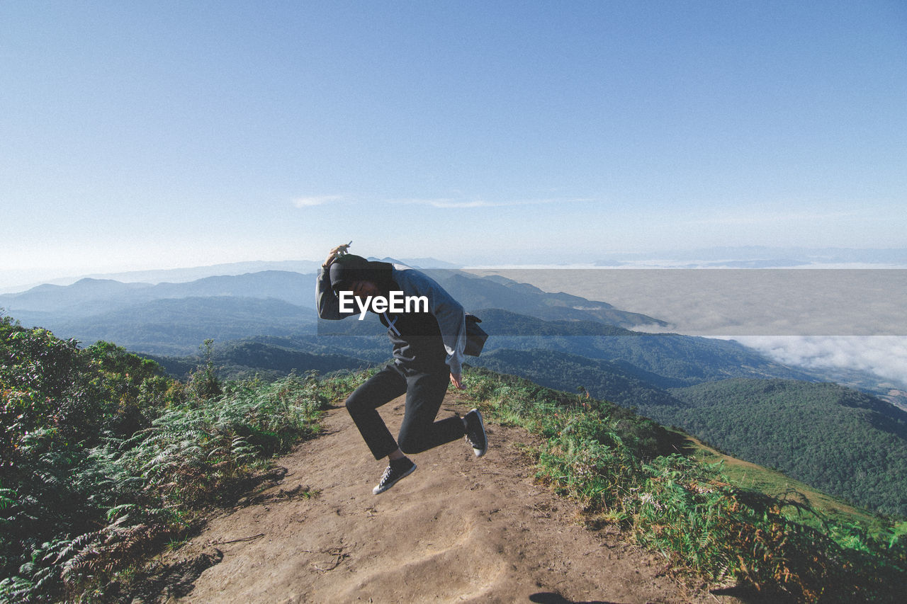 Man jumping over mountain against sky