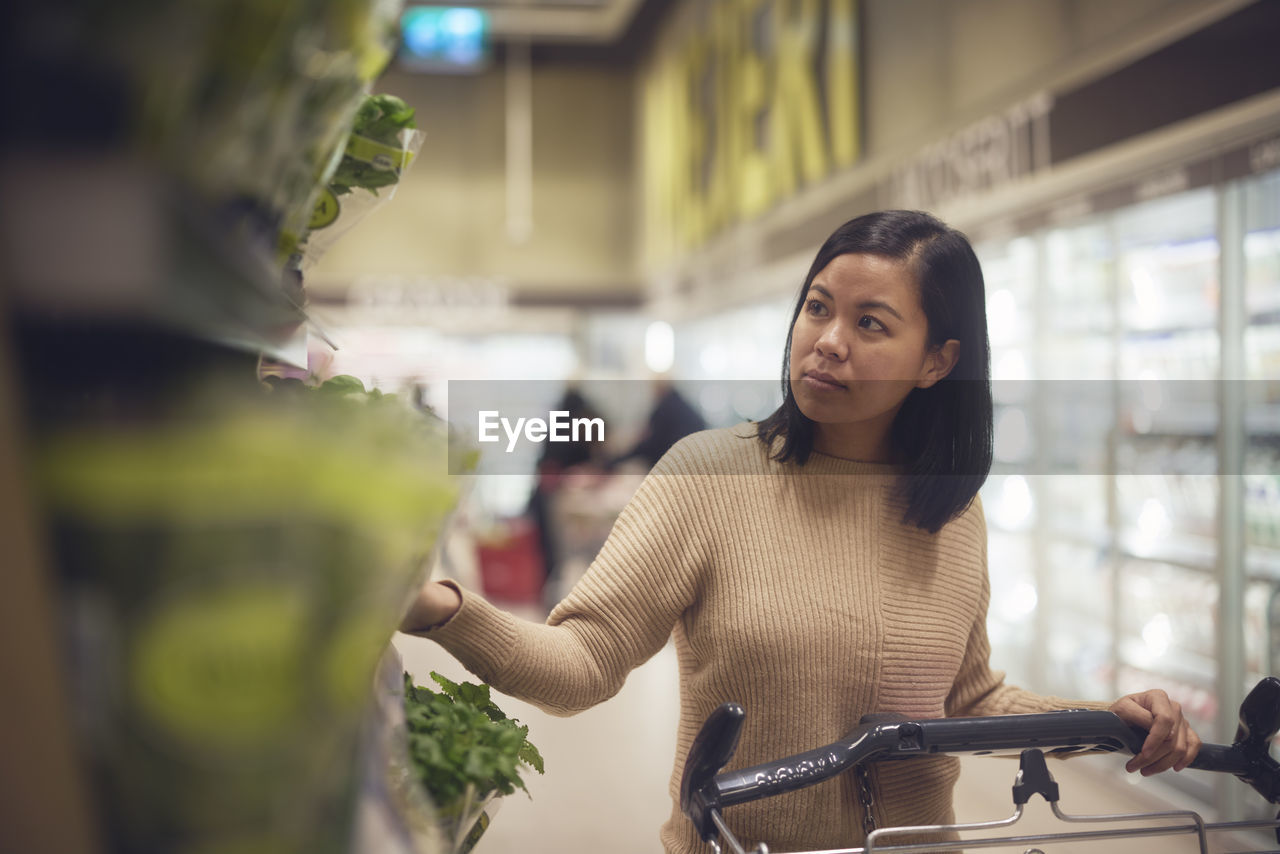 Woman in supermarket looking at fresh herbs while doing shopping