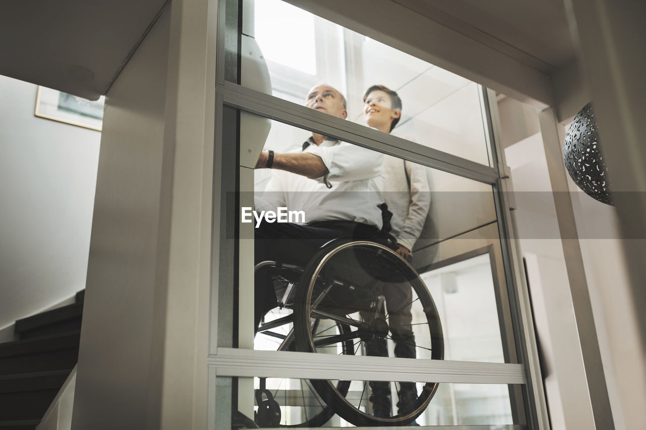Low angle view of son and father in wheelchair lift at home