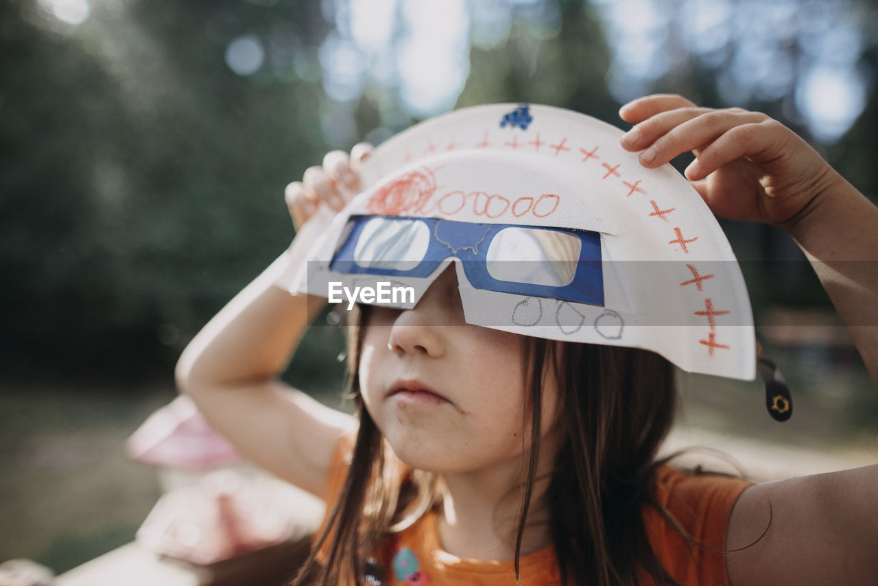 Girl holding solar eclipse glasses and mask while playing at park