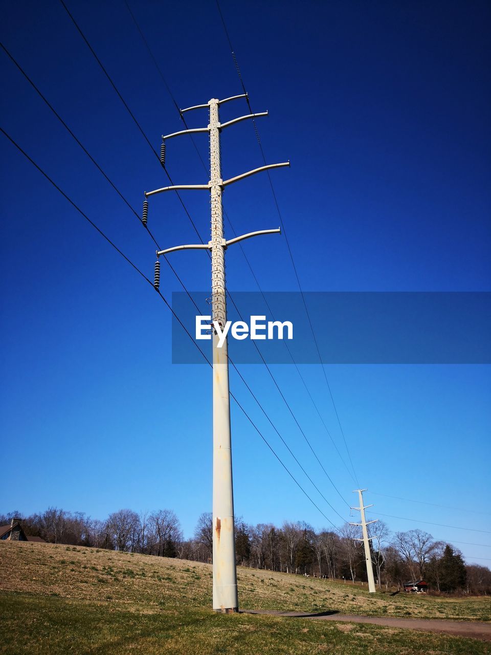 Low angle view of electricity pylon on field against clear blue sky