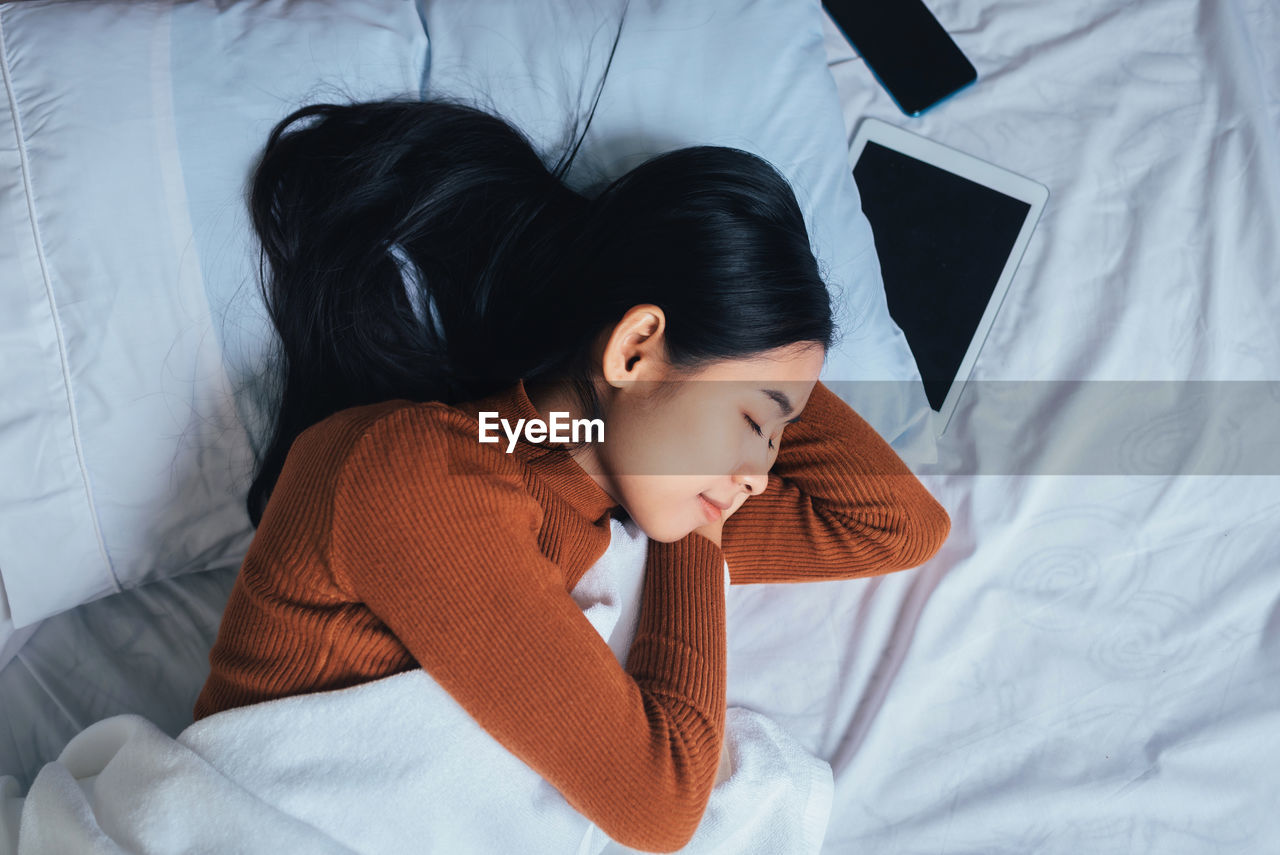 HIGH ANGLE VIEW OF WOMAN RESTING ON BED