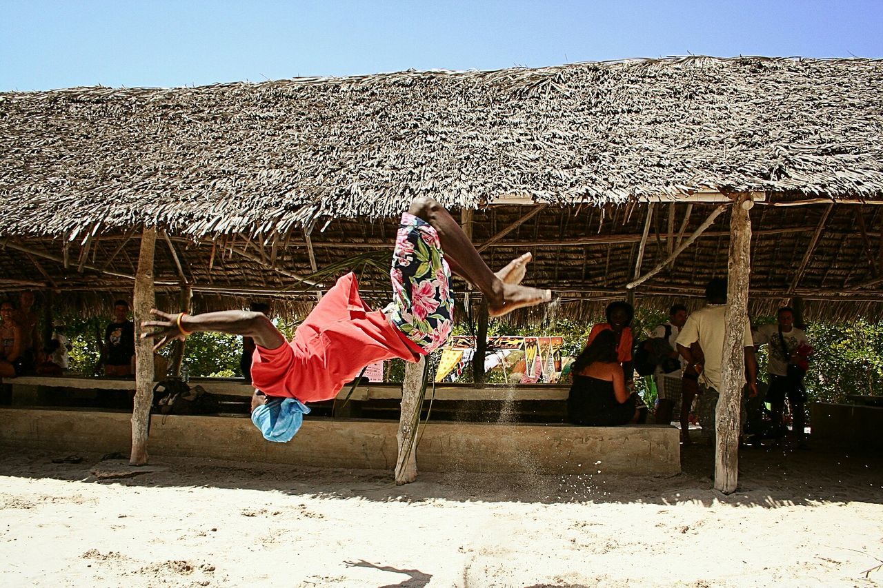 Full length of man doing somersault against hut during sunny day