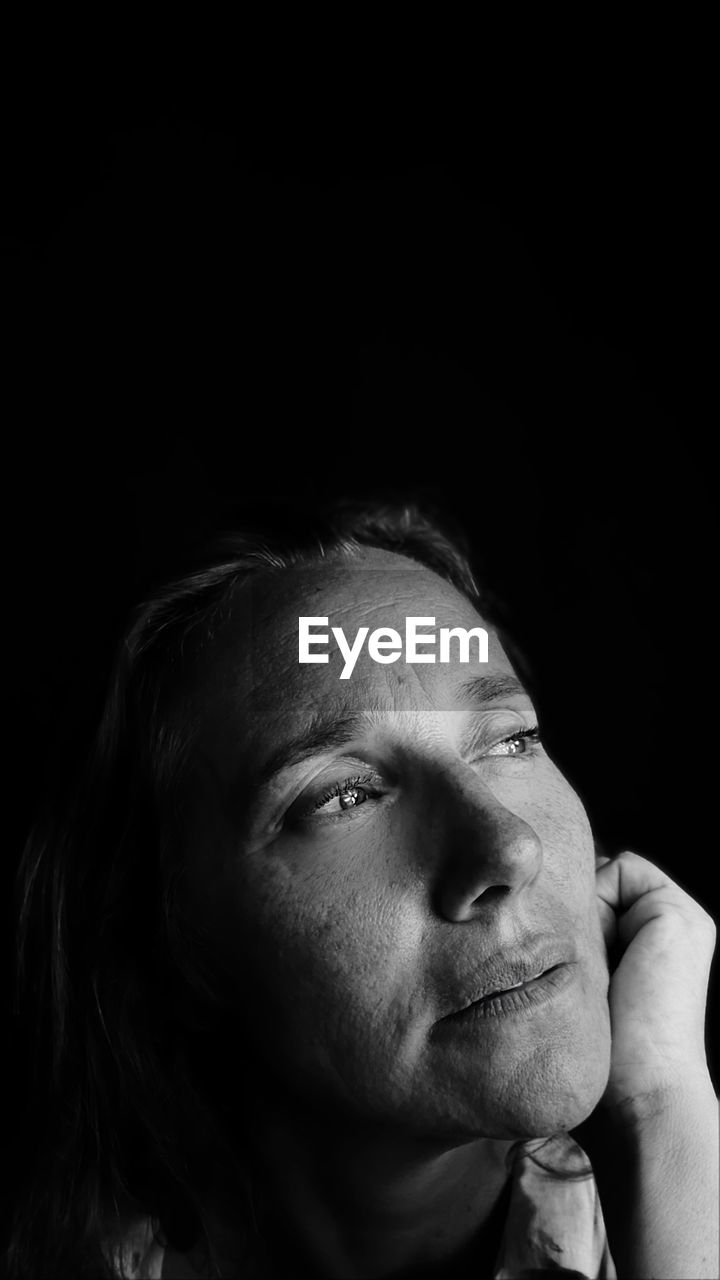 Close-up of thoughtful woman against black background