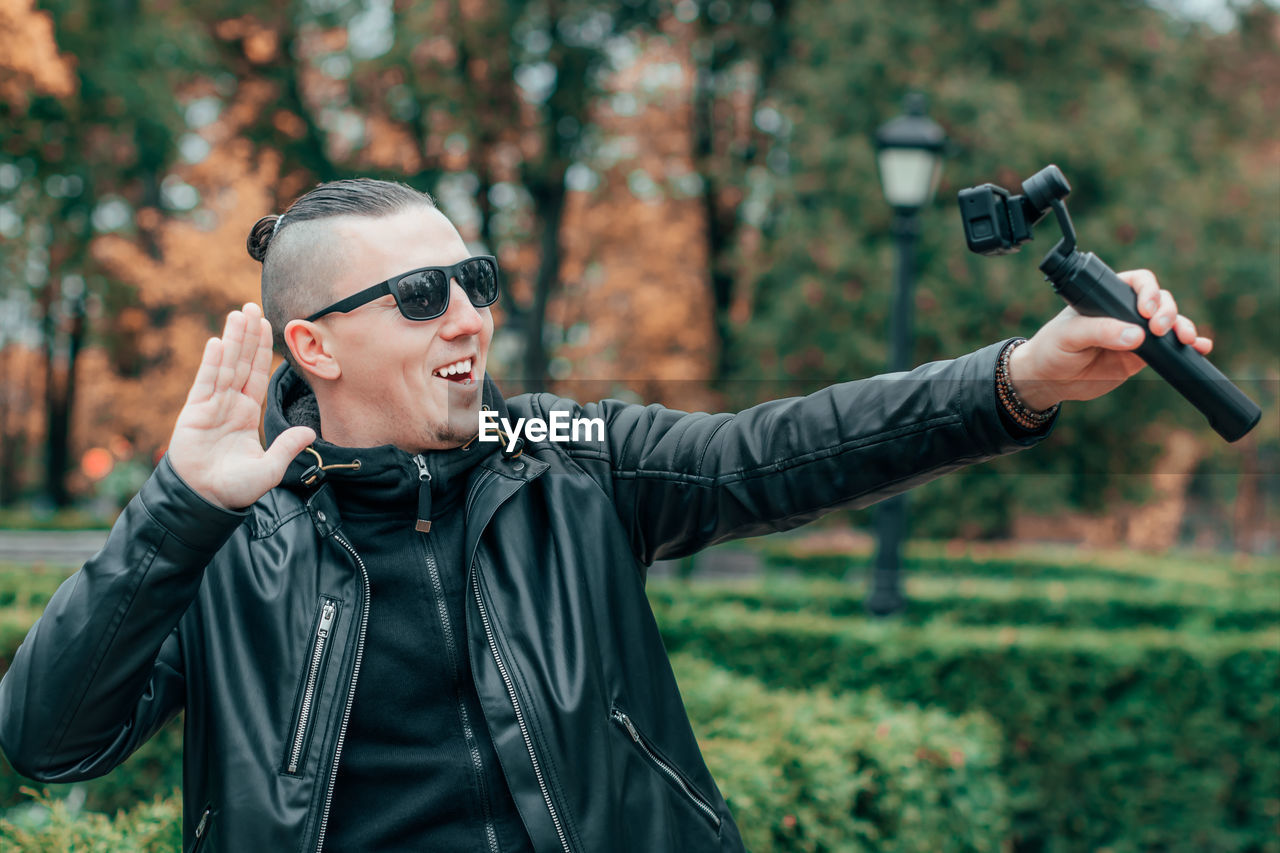 Young man wearing sunglasses filming with video camera in park