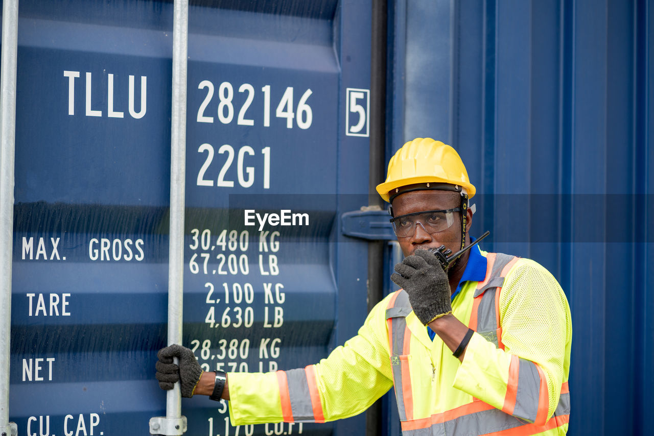 Engineer talking on walkie talkie standing by container