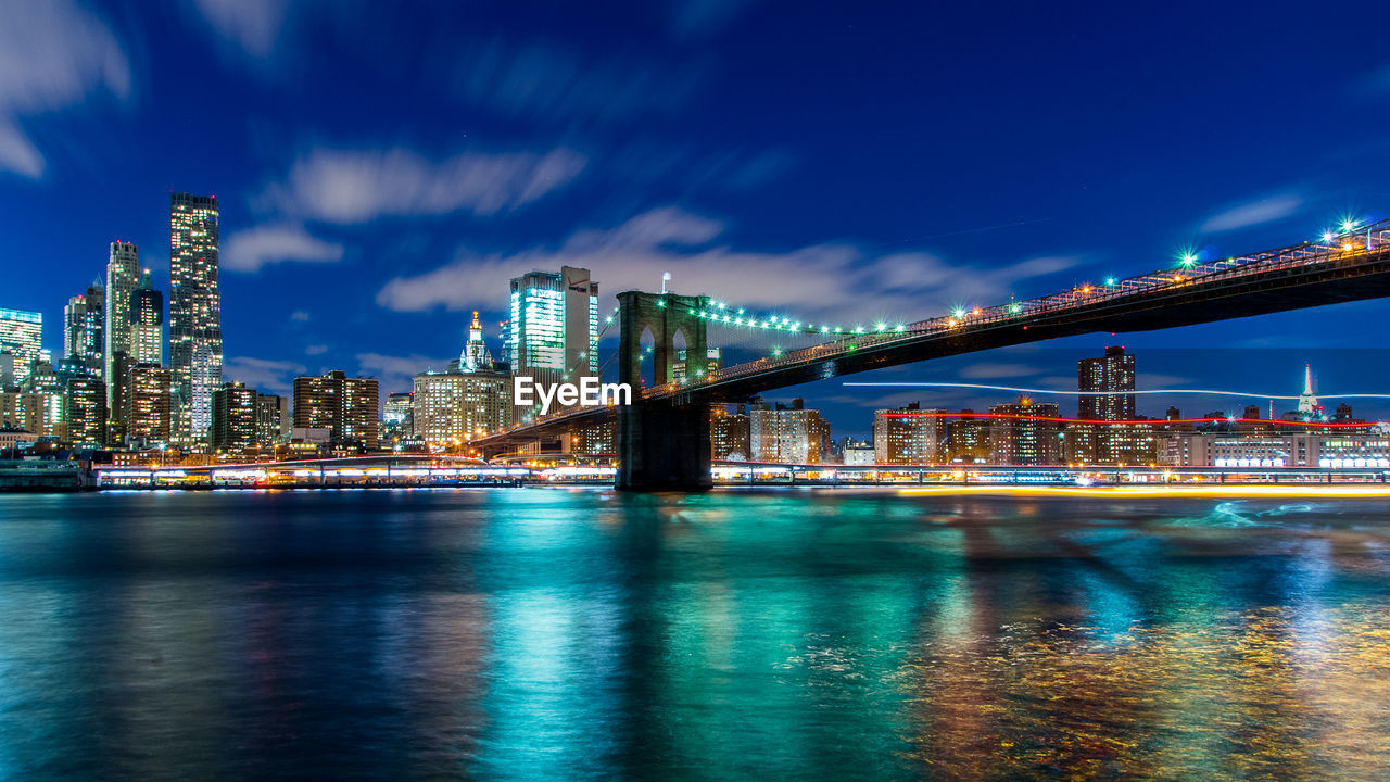 Illuminated brooklyn bridge over east river against sky at night