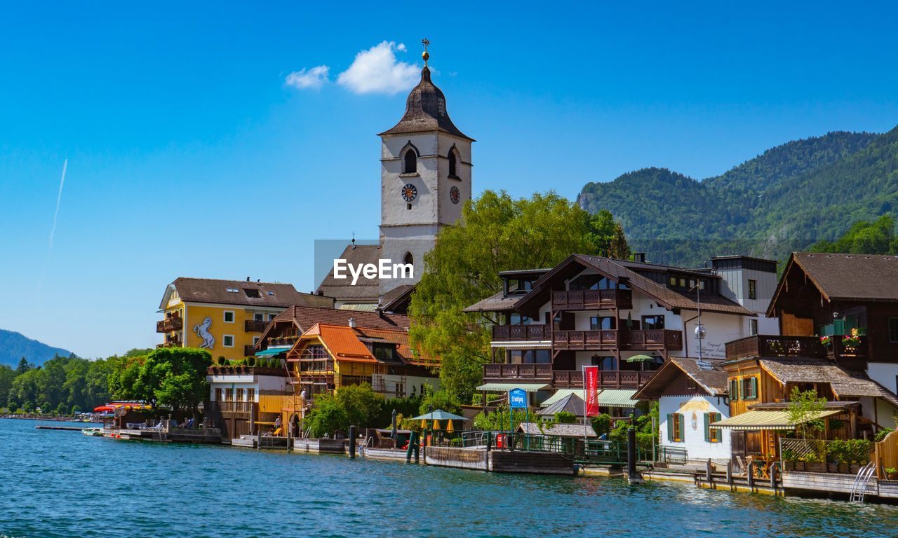 Buildings by river against blue sky