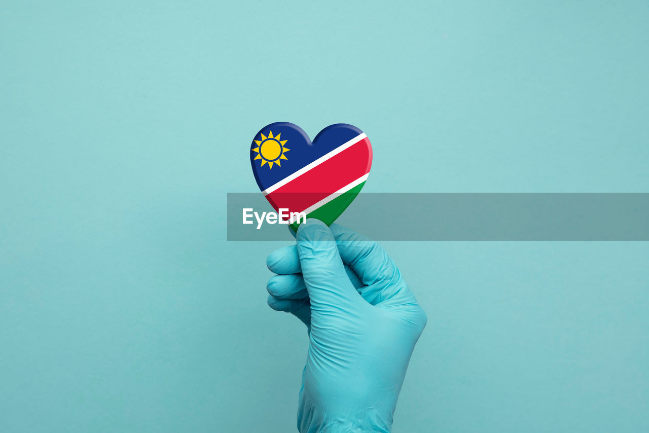 CLOSE-UP OF HAND HOLDING FLAG OVER BLUE BACKGROUND