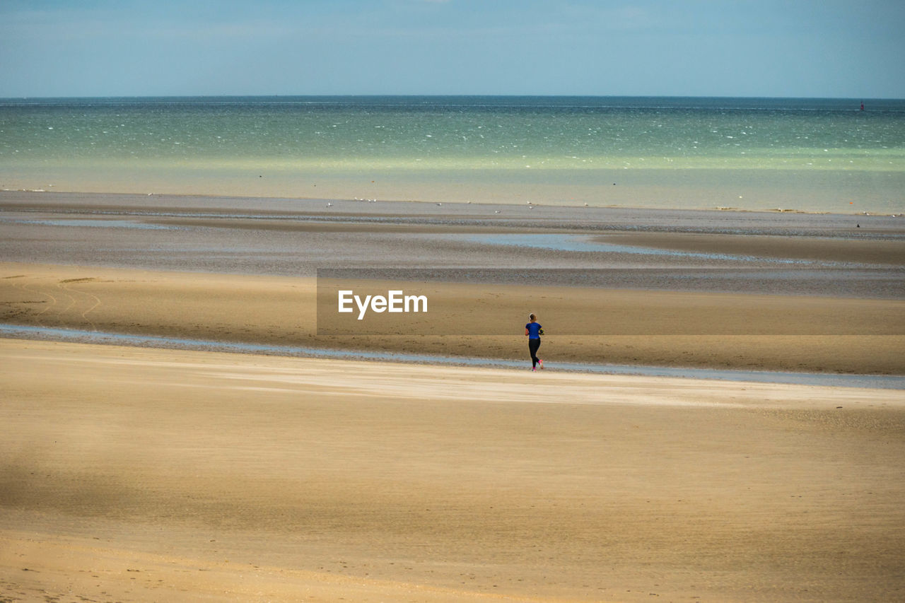 Rear view of woman running on sand at beach