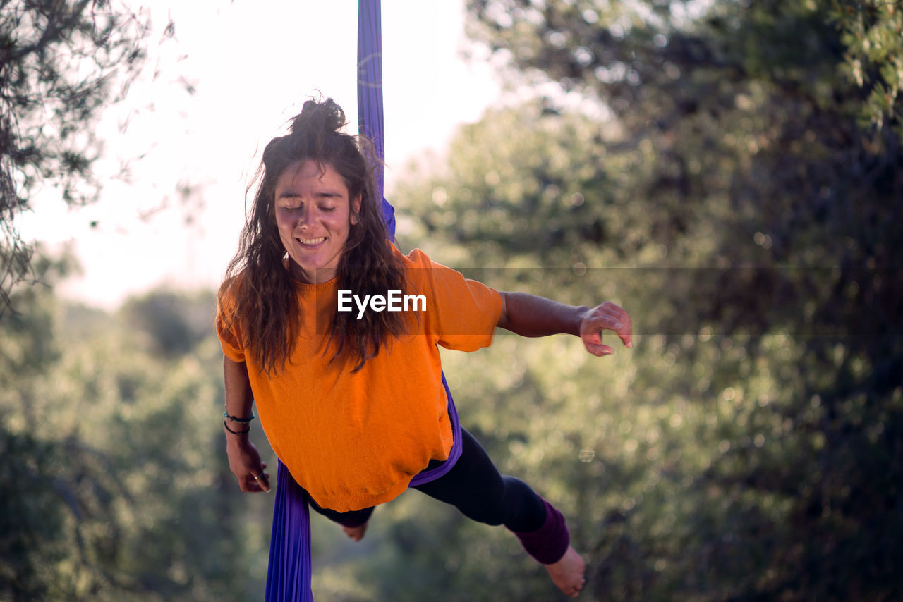 Young girl acrobat. practicing aerial silks. woman doing circus stunts with clothes in the forest. balance hip lock.