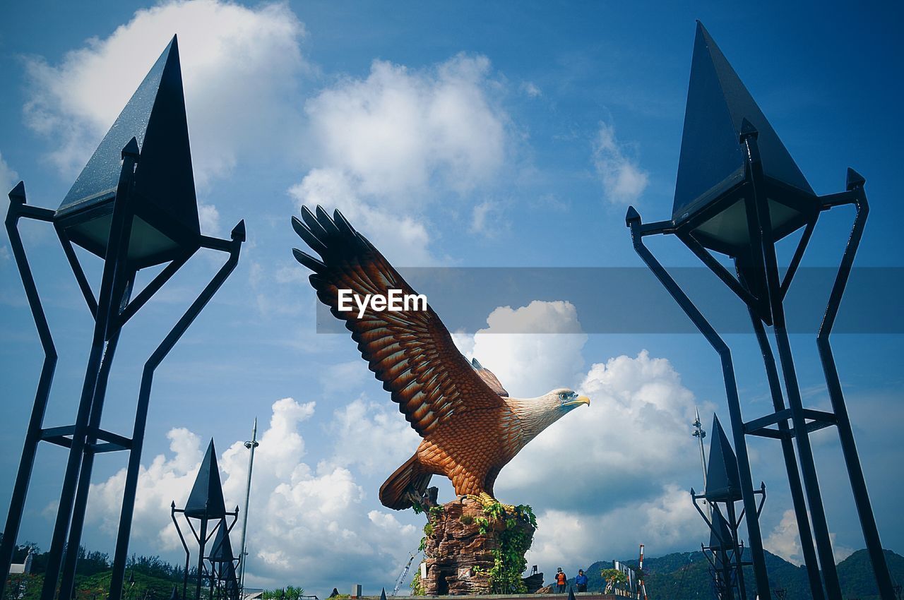 Low angle view of bird statue on blue sky and clouds