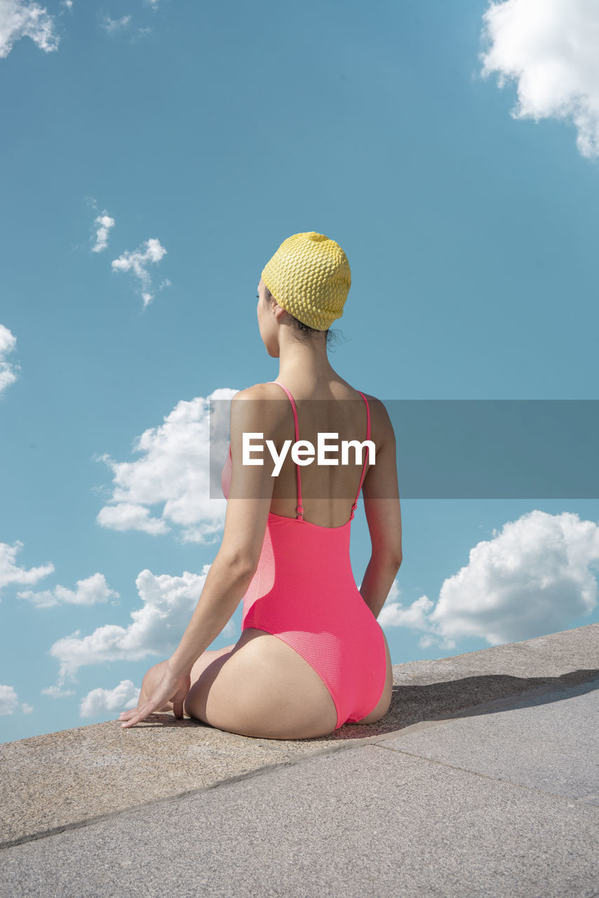 Woman with swimming cap and swimsuit sitting at edge