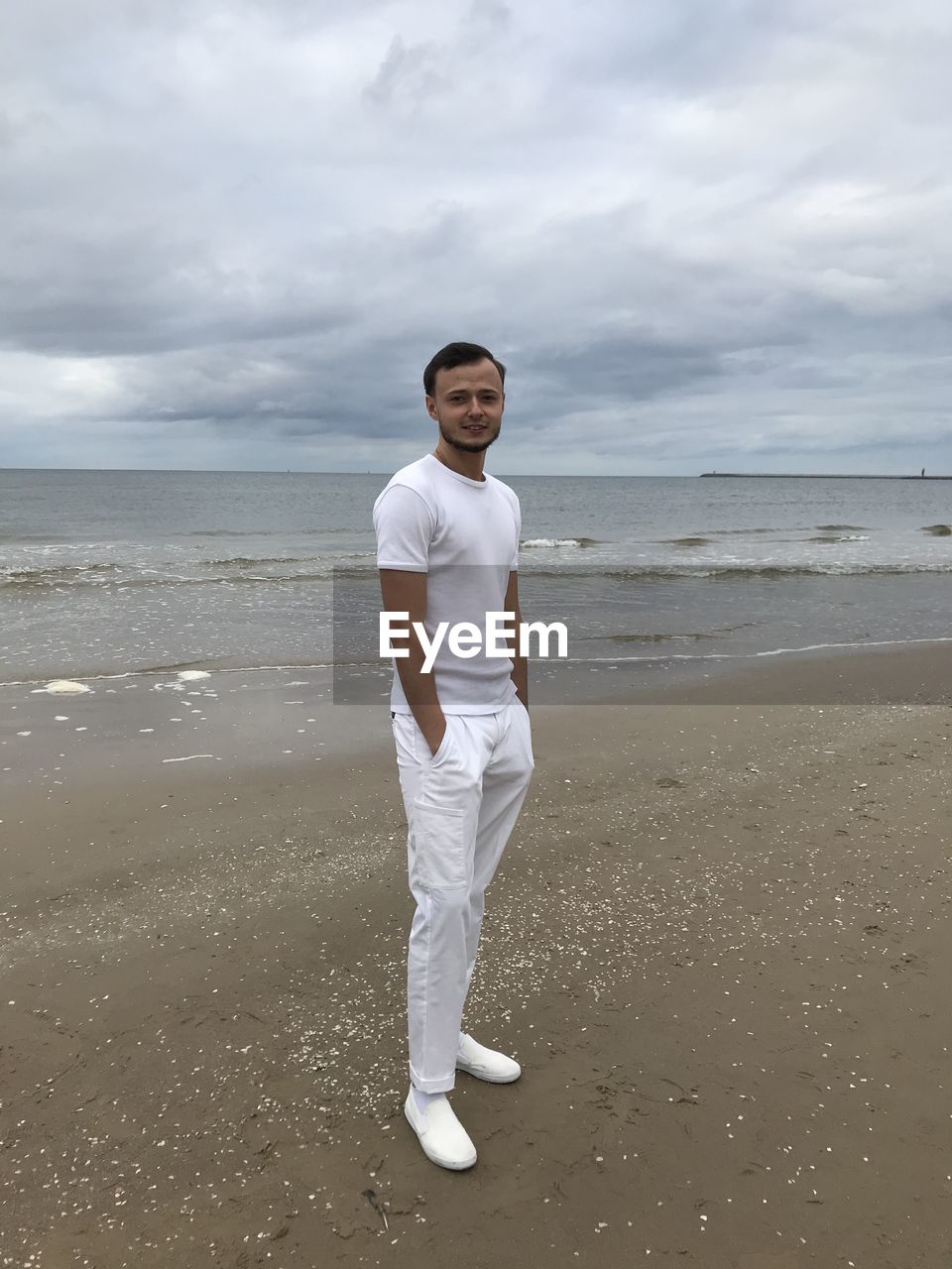 PORTRAIT OF MAN STANDING ON BEACH AGAINST SKY