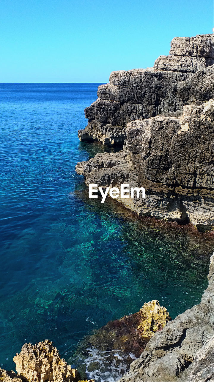 Rock formations in sea against clear blue sky