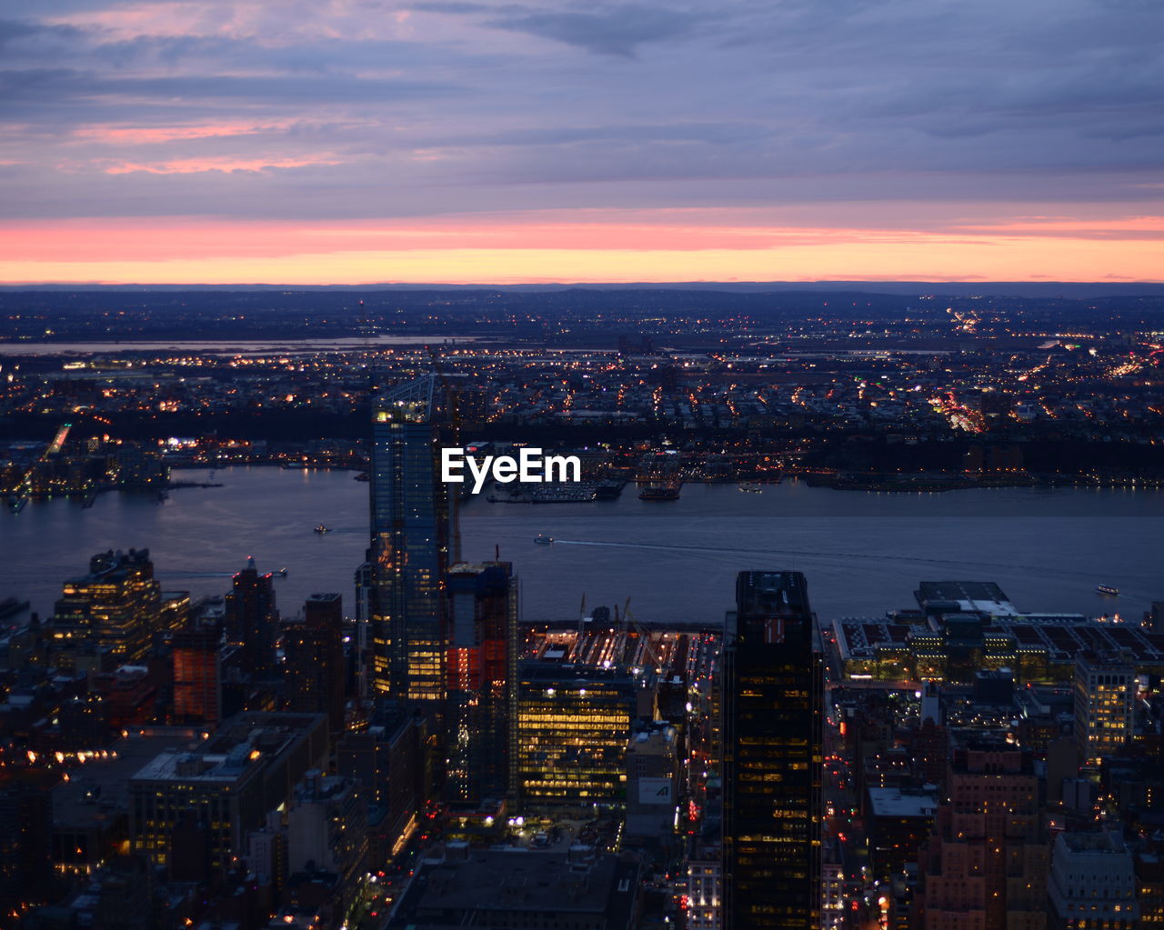 Aerial view of river amidst illuminated cityscape during sunset