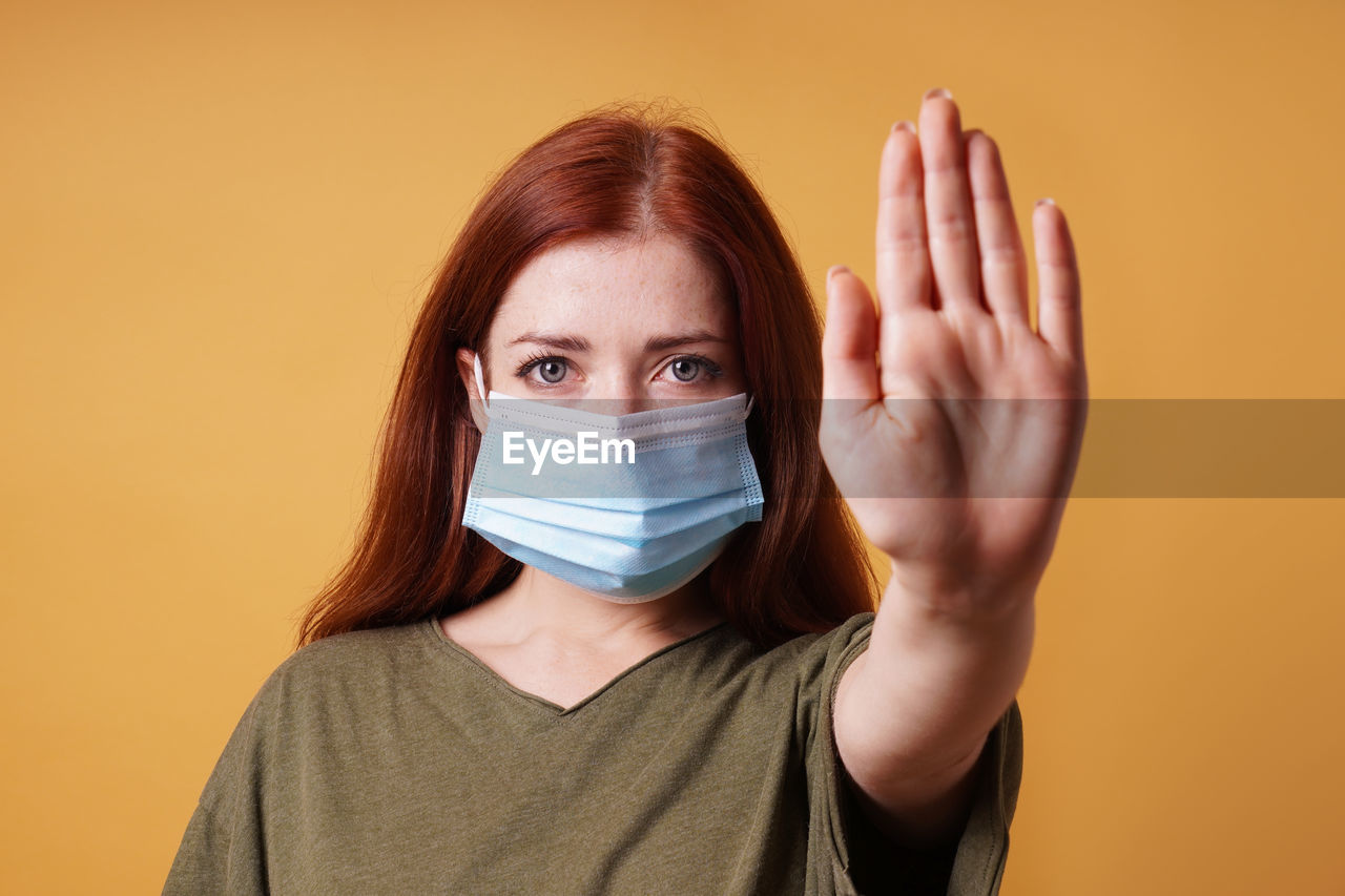 Young woman wearing medical face mask making stop hand gesture