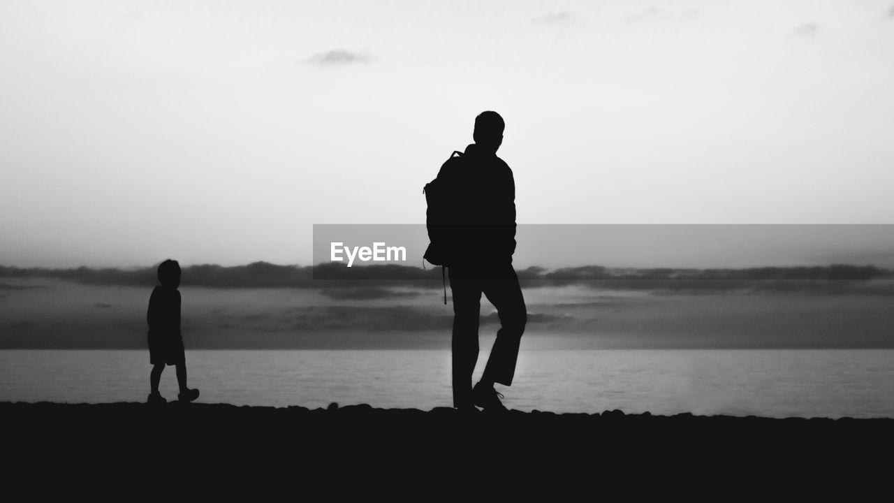 Silhouette men walking on beach against sky