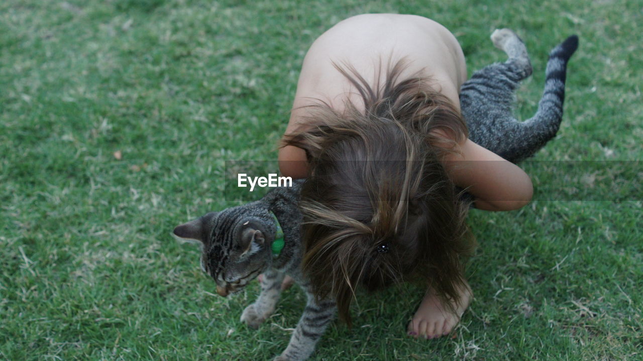 High angle view of shirtless girl hugging her pet cat on field