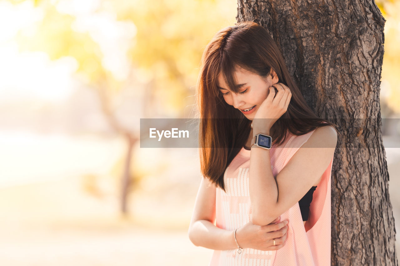 Beautiful young woman standing against tree trunk