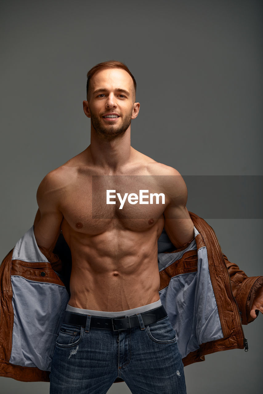 portrait of shirtless young man standing against black background