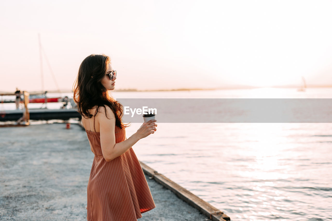 WOMAN HOLDING UMBRELLA WHILE STANDING AGAINST SEA