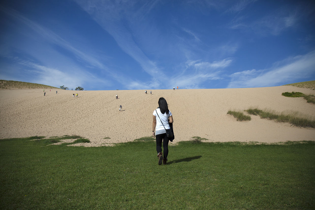 Rear view of woman walking on grassy field against sky