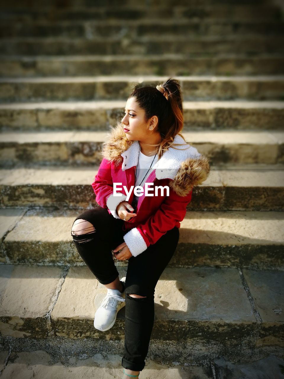 Thoughtful young woman wearing pink jacket while sitting on steps