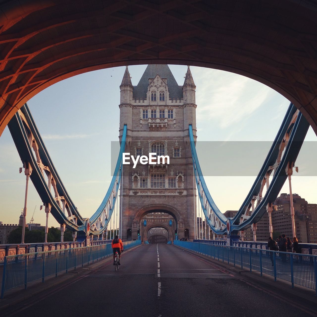 Rear view of cyclist riding bicycle on tower bridge against sky at morning