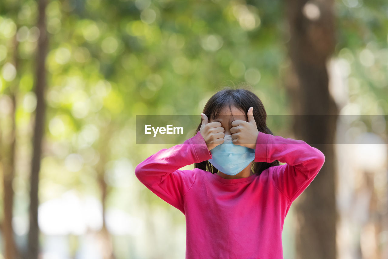 Cute girl wearing mask covering eyes while standing outdoors