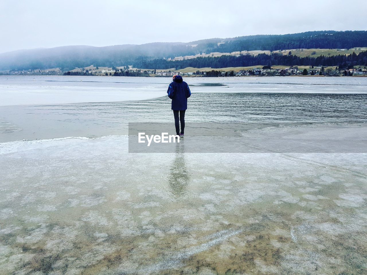 Rear view of man on frozen lake against sky