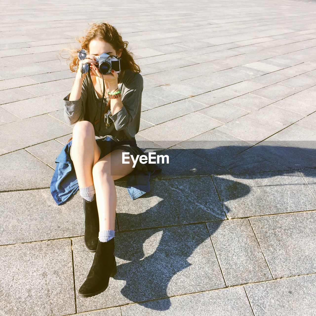 Young woman photographing while sitting on street