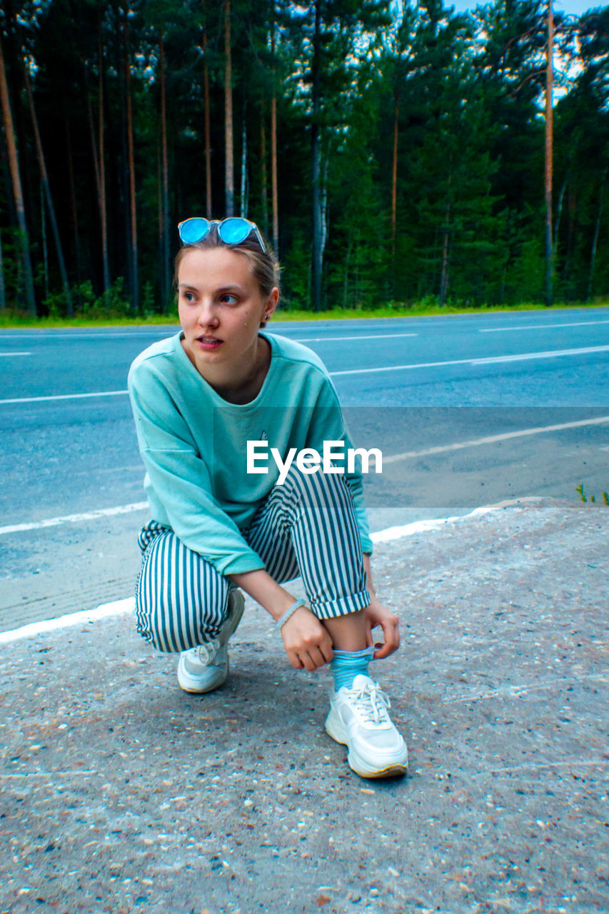 Young woman looking away while crouching on road