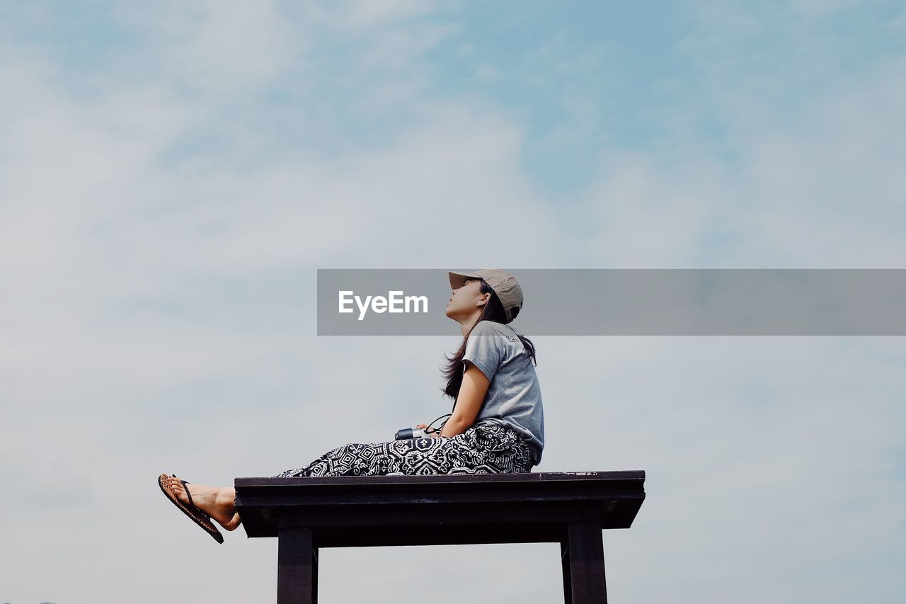 Low angle view of woman sitting on seat against sky