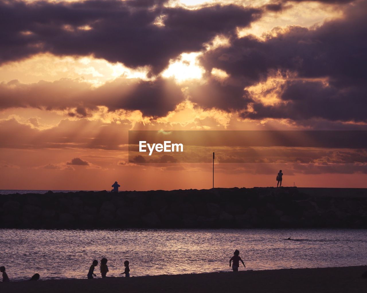 Silhouette children at beach against sky during sunset