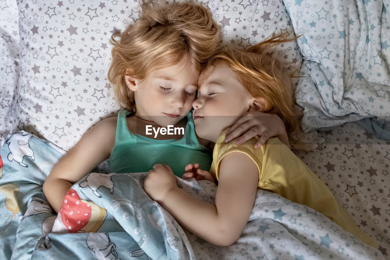 High angle view of sisters sleeping on bed at home