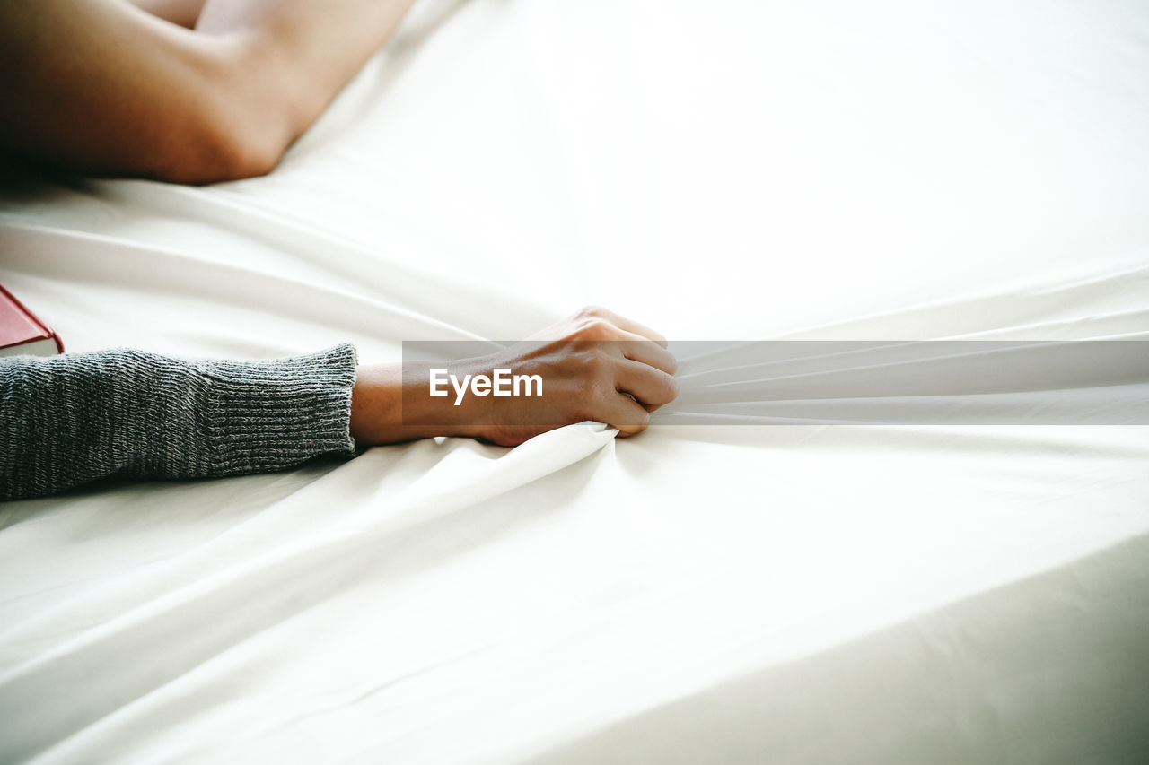 Cropped hand of woman holding blanket in bedroom