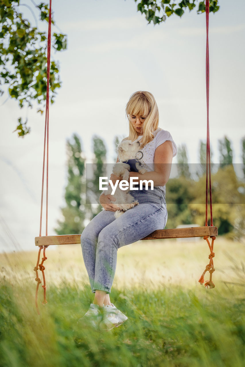 Young woman with a white dog on a tree swing.