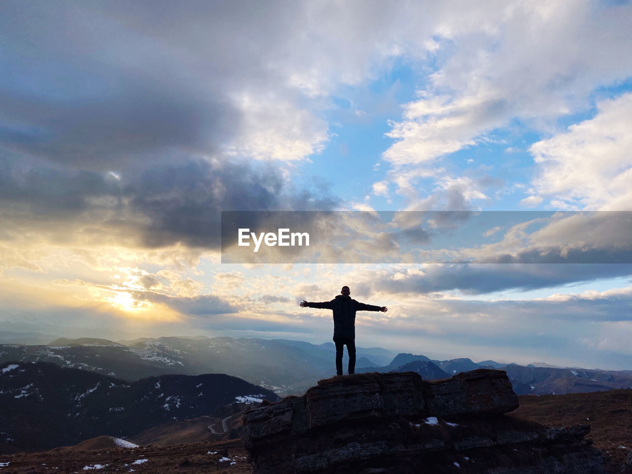 MAN STANDING ON ROCK AGAINST SKY AT SUNSET