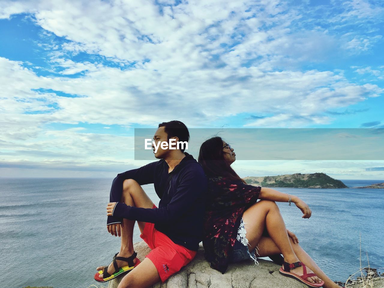 COUPLE SITTING ON BEACH AGAINST SKY