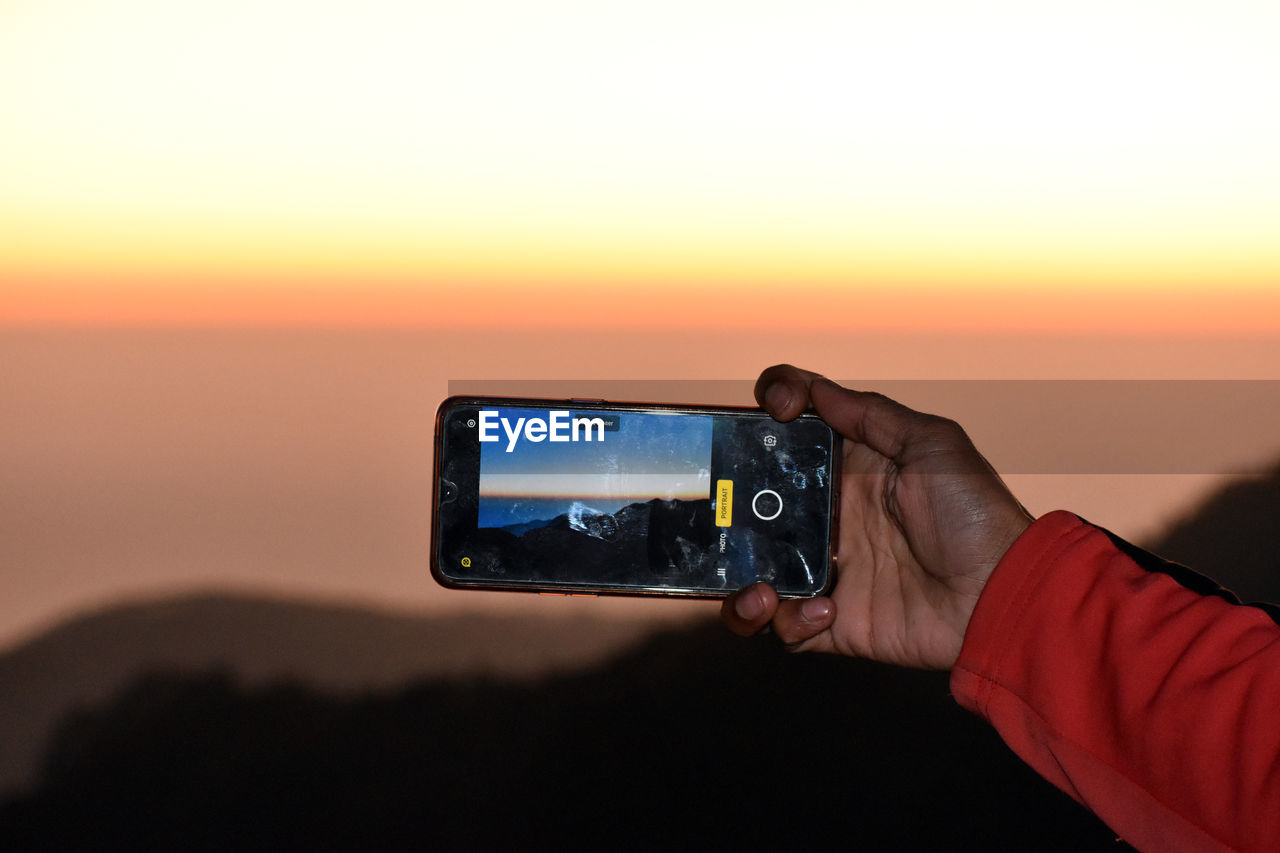 MAN PHOTOGRAPHING ON MOBILE PHONE AGAINST SKY