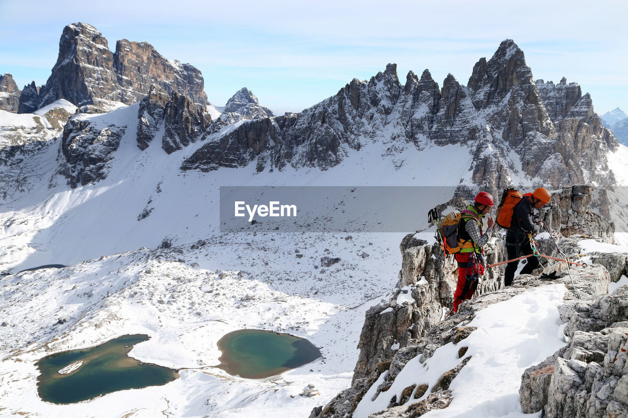 LOW ANGLE VIEW OF PEOPLE ON SNOWCAPPED MOUNTAIN AGAINST SKY