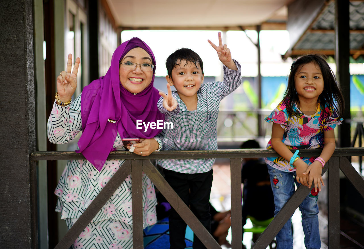 Portrait of smiling mother and children standing against railing